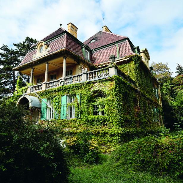 Ein mit Efeu bewachsenes, mehrstöckiges Haus mit einem Balkon und grünen Fensterläden.