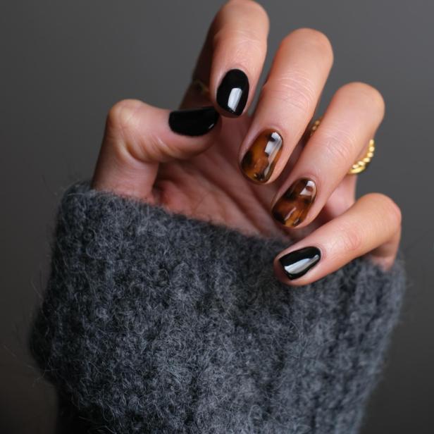 Hand mit braunem und schwarzem Nagellack.
