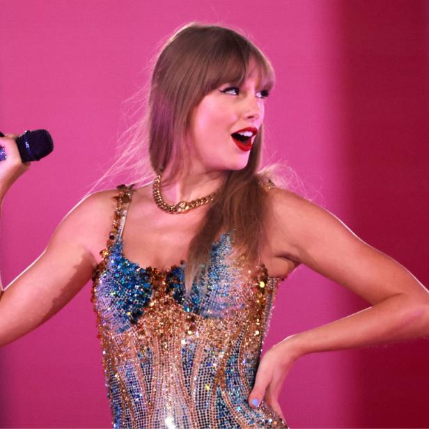 Taylor Swift auf der Bühne mit einem Mikro in der Hand, schaut verschmitzt.