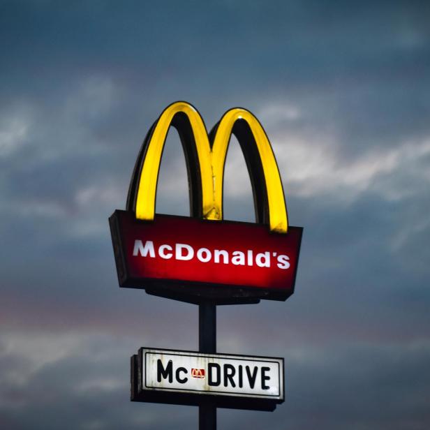 Ein McDonald's-Schild mit dem Schriftzug „McDrive“ vor einem bewölkten Himmel.