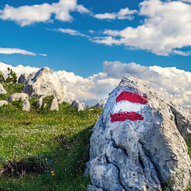 Ein Wegweiser mit rot-weiß-roter Markierung auf einem Felsen in den Bergen.