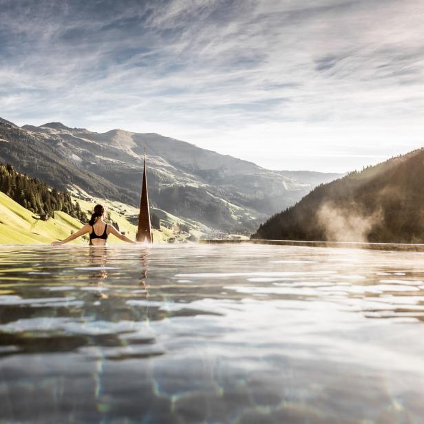 Eine Frau entspannt in einem Infinity-Pool mit Blick auf die Berge.