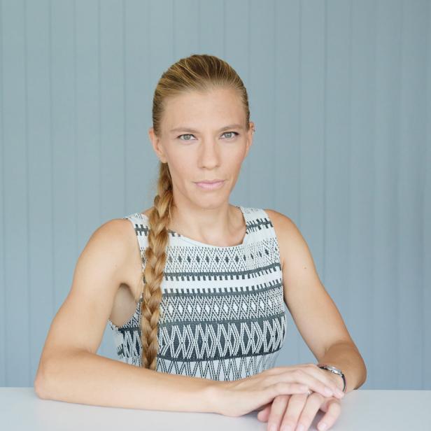 Eine Frau mit blonden Haaren und einem gemusterten Kleid sitzt an einem Tisch.