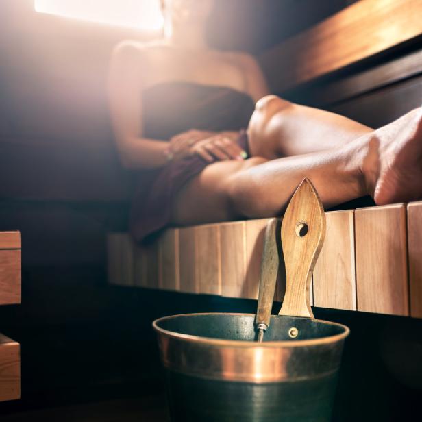 Eine Frau entspannt eingewickelt in ein Tuch in einer Sauna.