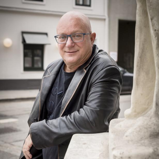 Ein Mann mit Brille und Lederjacke lehnt an einem steinernen Geländer.