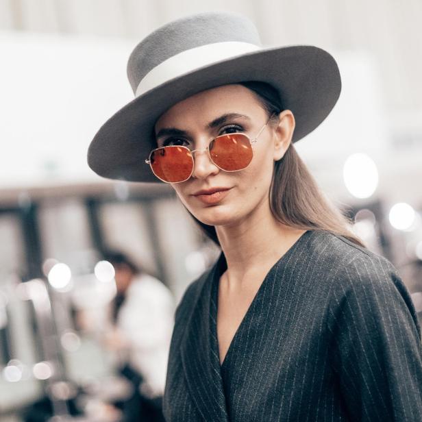Eine Frau mit Hut und orangefarbener Sonnenbrille blickt in die Kamera.