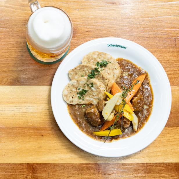 Bierfleisch mit Semmelknödeln und Gemüse auf einem Teller des Schweizerhauses, dazu ein Bier.