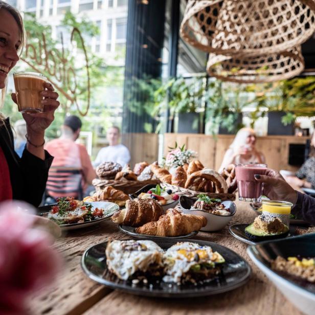 Eine Frau genießt ein reichhaltiges Frühstück mit Croissants und belegten Broten in einem Restaurant.