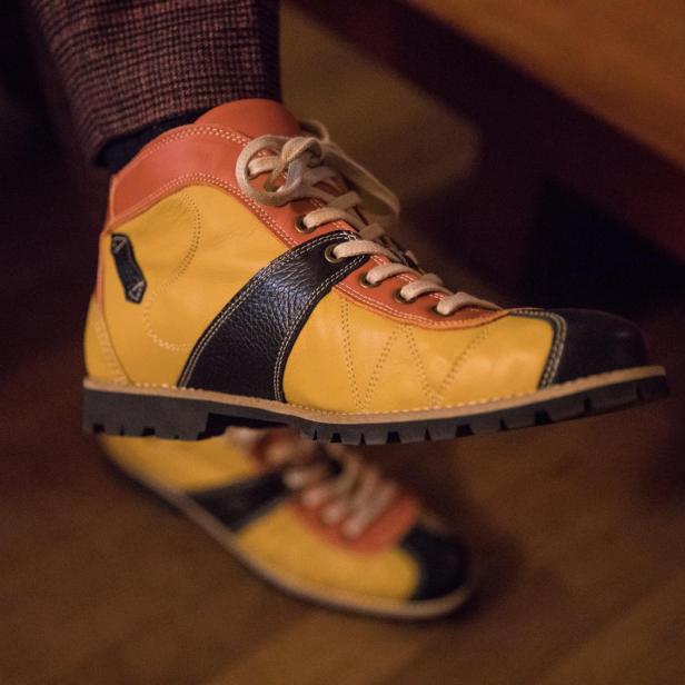 Ein gelb-orangefarbener Lederschuh mit schwarzen Akzenten wird präsentiert.