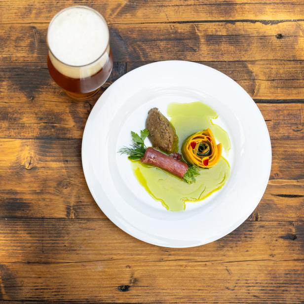 Ein Teller mit kunstvoll angerichteten Speisen und einem Glas Bier auf einem Holztisch.