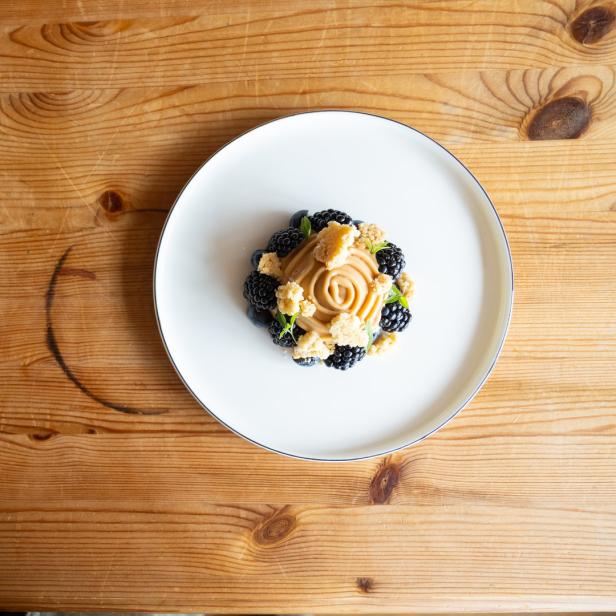 Ein Dessertteller mit Brombeeren, Blaubeeren und einer Karamellcreme auf einem Holztisch.