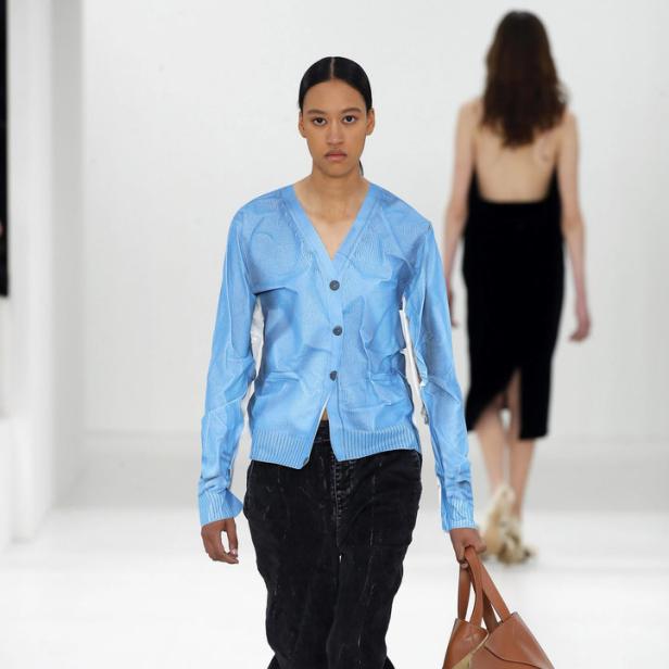 Ein Model präsentiert eine blaue Weste und eine große braune Ledertasche von Loewe.
