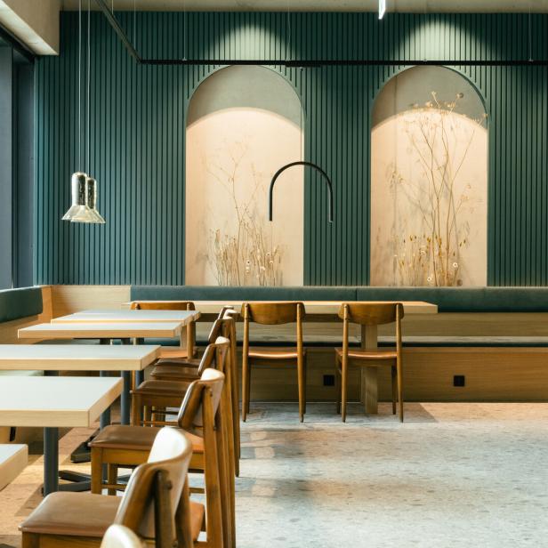 Innenansicht eines Cafés mit Tischen, Stühlen und einer grünen Akzentwand.