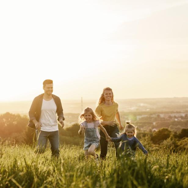 Eine Familie rennt über eine Wiese im goldenen Abendlicht.