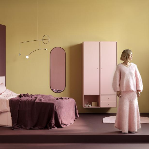 Ein rosa Schlafzimmer mit einem Bett, einem Schrank und einer Frau in einem rosa Outfit.