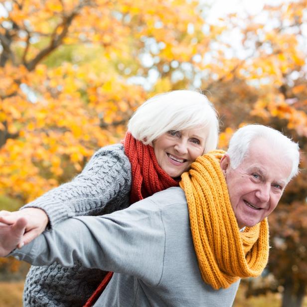 Ein älteres Paar hat Spaß im Herbstlaub, die Frau reitet Huckepack.