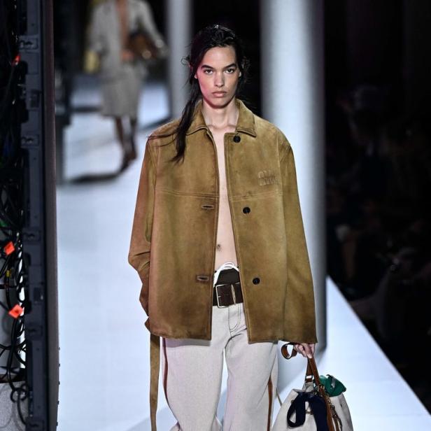 Ein Model auf dem Laufsteg, gekleidet in eine Jacke, weite Hose und Loafer, mit einer Tasche in der Hand.