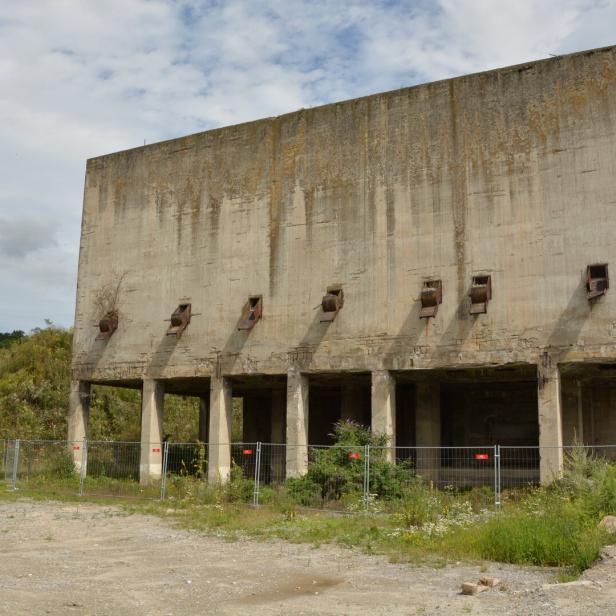 Ein großes, verlassenes Betongebäude mit mehreren Öffnungen steht auf einem Feld.
