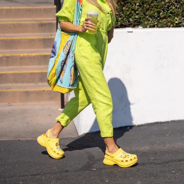 Heidi Klum in einem hellgrünen Overall, gelben Crocs und mit einer bunten Tasche über der Schulter.
