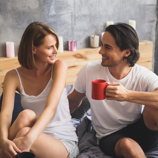 Ein Paar sitzt im Bett und trinkt Kaffee.