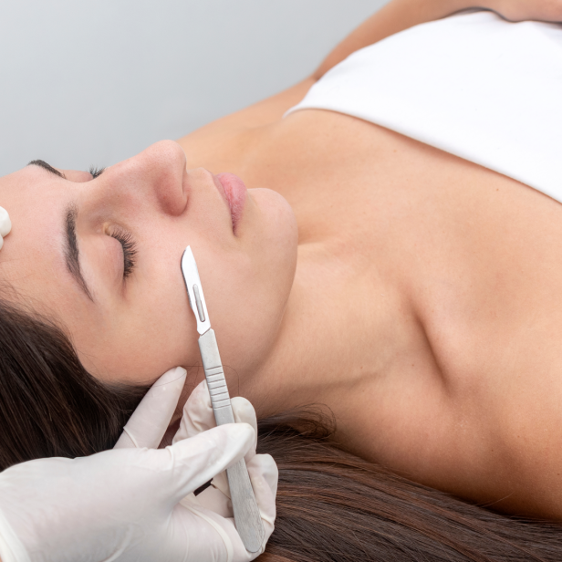 Eine Kosmetikerin führt eine Dermaplaning-Behandlung mit einem Skalpell auf dem Gesicht einer Frau durch.