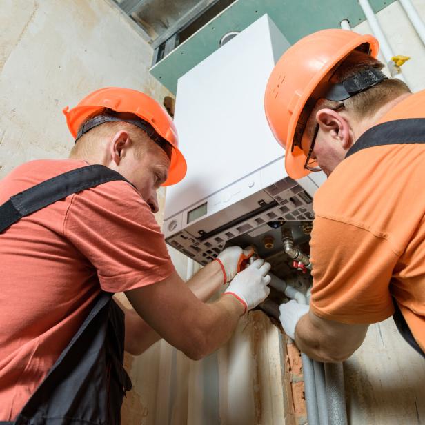 Workers are connecting the pipes to the gas boiler.