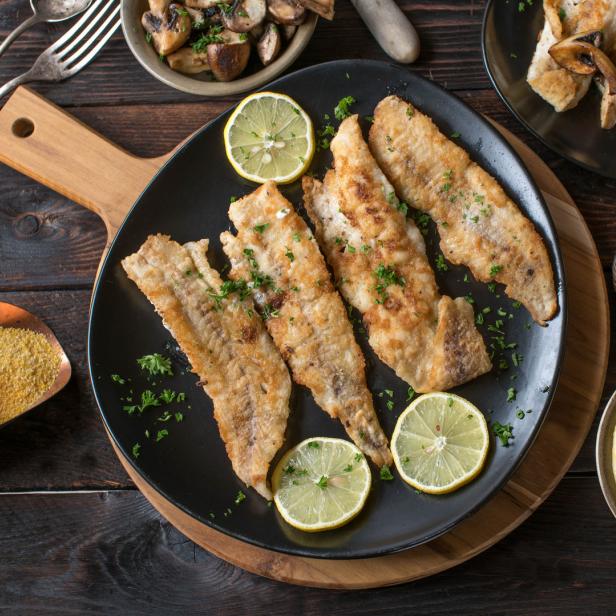 Gebratene Fischfilets mit Zitrone, Kräutern und Pilzen auf einem Teller angerichtet.