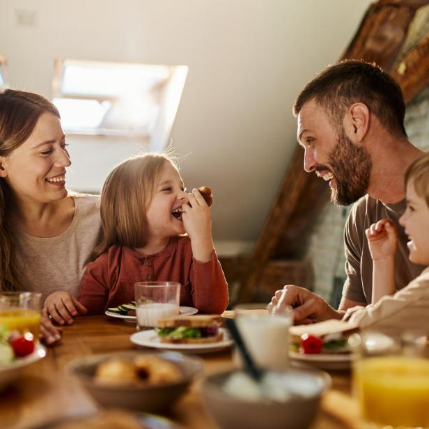 Eine Familie sitzt lachend beim Essen an einem Tisch.