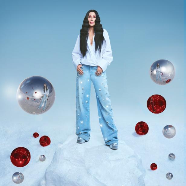 Cher steht auf einer schneebedeckten Oberfläche, umgeben von roten und silbernen Kugeln.
