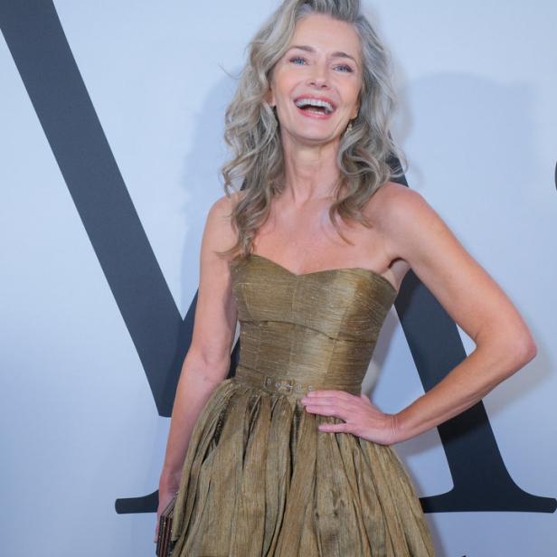 Eine Frau in einem goldenen, trägerlosen Kleid lächelt auf dem roten Teppich.