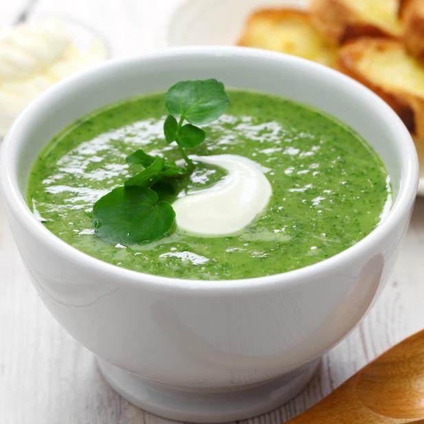 Eine Schüssel mit grüner Cremesuppe, garniert mit einem Klecks Sahne und Brunnenkresse.