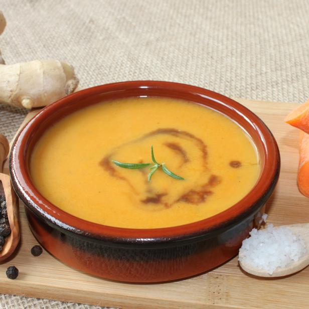 Eine Schüssel Kürbissuppe mit Ingwer, Karotten, Pfeffer und Salz auf einem Holzbrett.