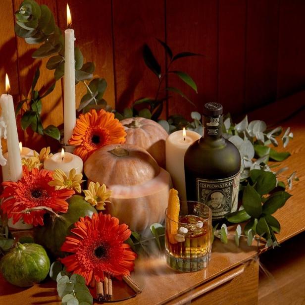 Dekorative Herbstszene mit Kürbissen, Gerbera, Kerzen und einer Flasche Diplomático Rum.