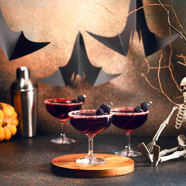 Halloween-Szene mit Cocktails, Kürbissen, Fledermäusen und einem Skelett.