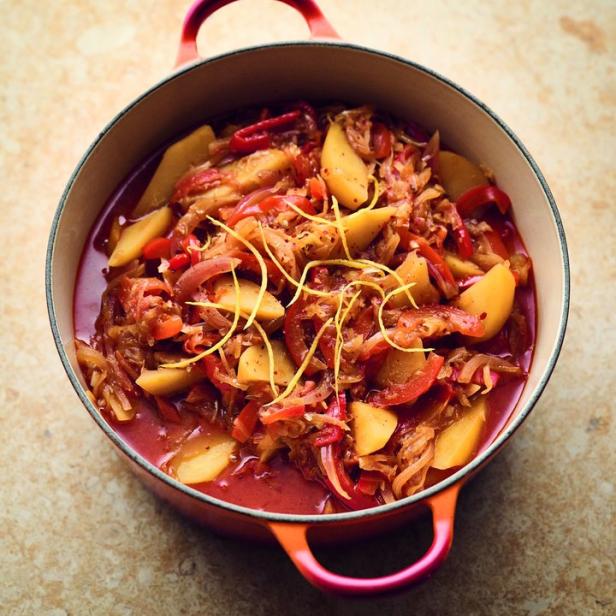 Ein roter Topf gefüllt mit einem Gericht aus Kartoffeln, Paprika und Zwiebeln, garniert mit Zitronenzesten.