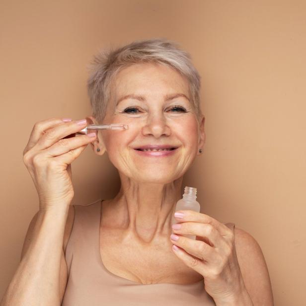 Eine ältere Frau trägt ein Serum mit einer Pipette auf ihr Gesicht auf.