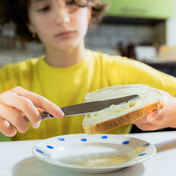 Ein Mädchen streicht Butter auf eine Scheibe Toastbrot.