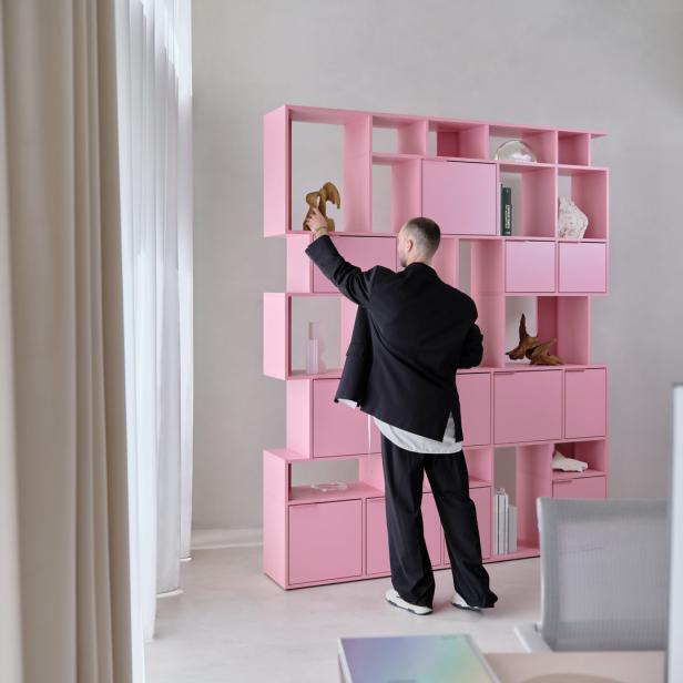 Ein Mann arrangiert Dekorationen in einem rosa Regal.