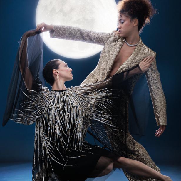 Zwei Frauen in glitzernden Kleidern posieren vor einem großen Mond.