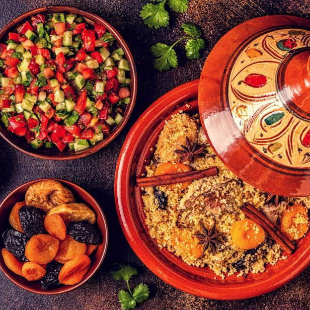 Ein Tajine mit Couscous, Trockenfrüchten und Gewürzen, zusammen mit Salat und Granatapfel.