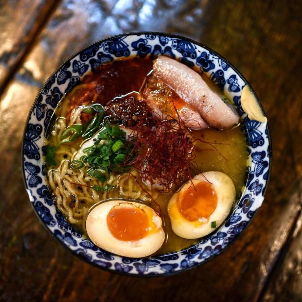 Eine Schüssel Ramen mit Eiern, Fleisch und Gemüse auf einem Holztisch.