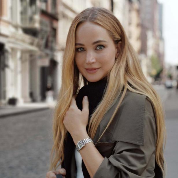 Jennifer Lawrence trägt einen Trenchcoat und eine Uhr auf einer Straße.