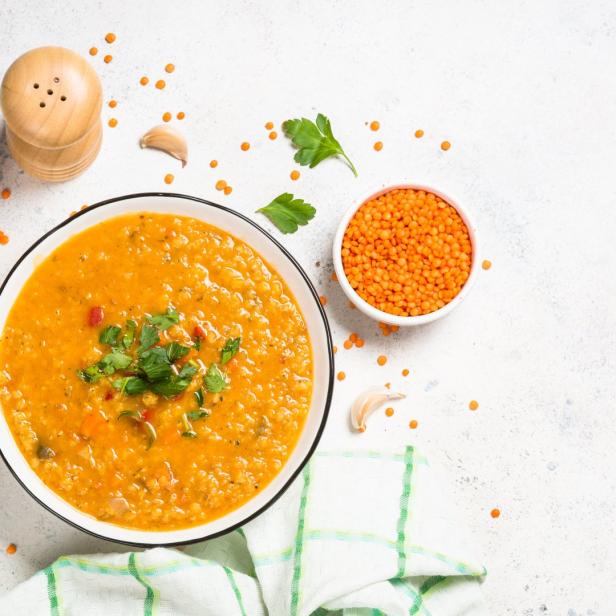 Eine Schüssel Linsensuppe mit Petersilie auf einem hellen Tisch.
