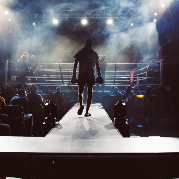 Ein Boxer auf dem Weg Richtung Boxring; links und rechts von ihm sitzt das Publikum