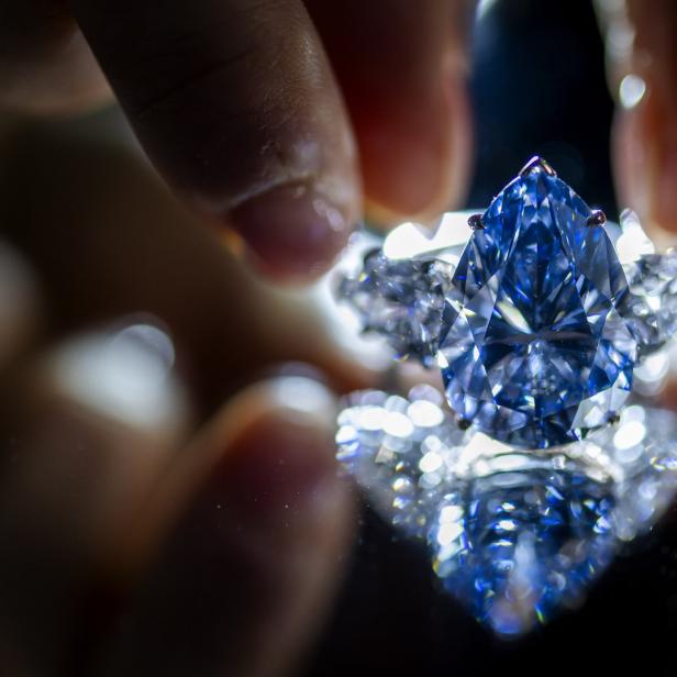 Ein tropfenförmiger blauer Diamant wird von Fingern gehalten.