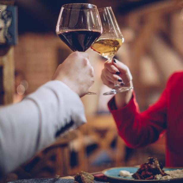 Ein Paar stößt mit Rot- und Weißwein in einem Restaurant an.