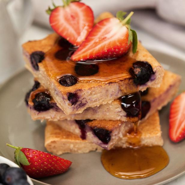 Ein Stapel Blaubeerpfannkuchen mit Erdbeeren und Sirup auf einem Teller.