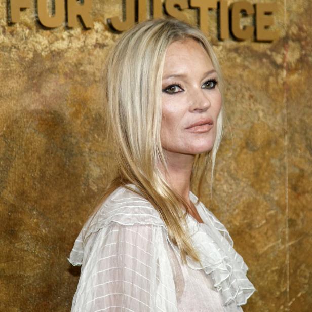 Kate Moss posiert vor einer Wand mit der Aufschrift „For Justice“.