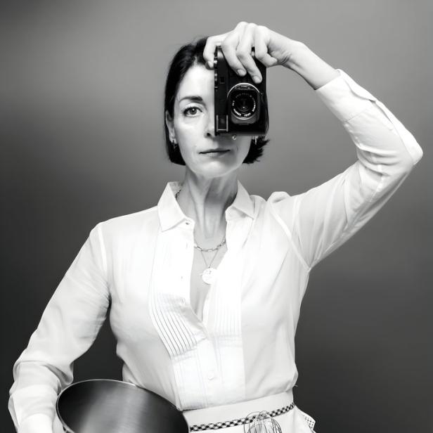 Mary McCartney hält eine Kamera vor ihr Auge und trägt eine Schürze mit Kochutensilien.