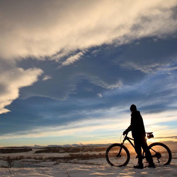 Ein Mountainbiker steht im Winter mit seinem Fahrrad im Schnee.